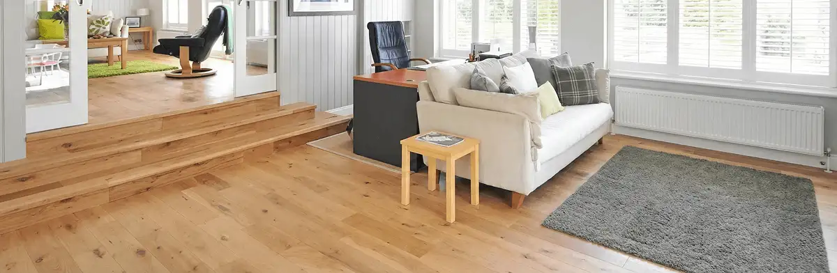A modern living room with professionally installed laminate flooring, a beige sofa, a small side table, a gray rug, and large windows with white shutters in Jersey City, NJ
